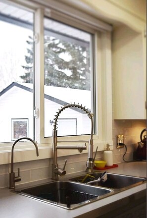 A kitchen with a stainless steel sink, a window, and a view of trees outside.
