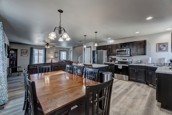 Kitchen with full complement of stainless steel appliances, cookware, bakeware, and large dining room table with seating for 8-10 people.