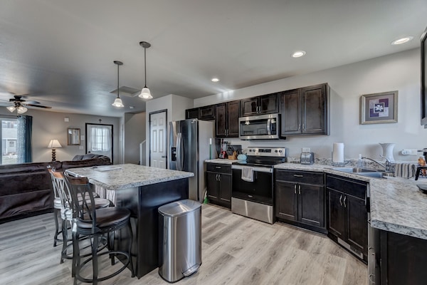 Kitchen with full complement of stainless steel appliances, cookware, bakeware, and large dining room table with seating for 8-10 people.