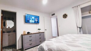 A bedroom with a bed, a dresser, a television mounted on the wall, and a door leading to another room. - Clean & quiet retreat with private backyard near shopping & trails. (Tucson)