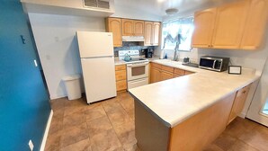 A compact kitchen with a refrigerator, stove, microwave, and wooden cabinets. - Clean & quiet retreat with private backyard near shopping & trails. (Tucson)