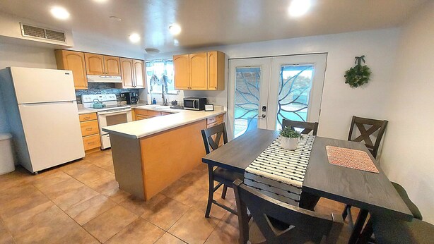 A compact kitchen with a refrigerator, stove, microwave, and wooden cabinets. - Clean & quiet retreat with private backyard near shopping & trails. (Tucson)