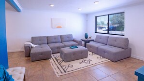 A living room with a sectional sofa, ottoman, and a small table with a vase. - Clean & quiet retreat with private backyard near shopping & trails. (Tucson)