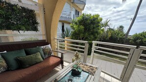 A balcony with a sofa and a table, surrounded by a white railing, with a view of greenery and a building in the background. - Studio "Entre Terre et Mer" Residence Anse des Sables (Marigot)