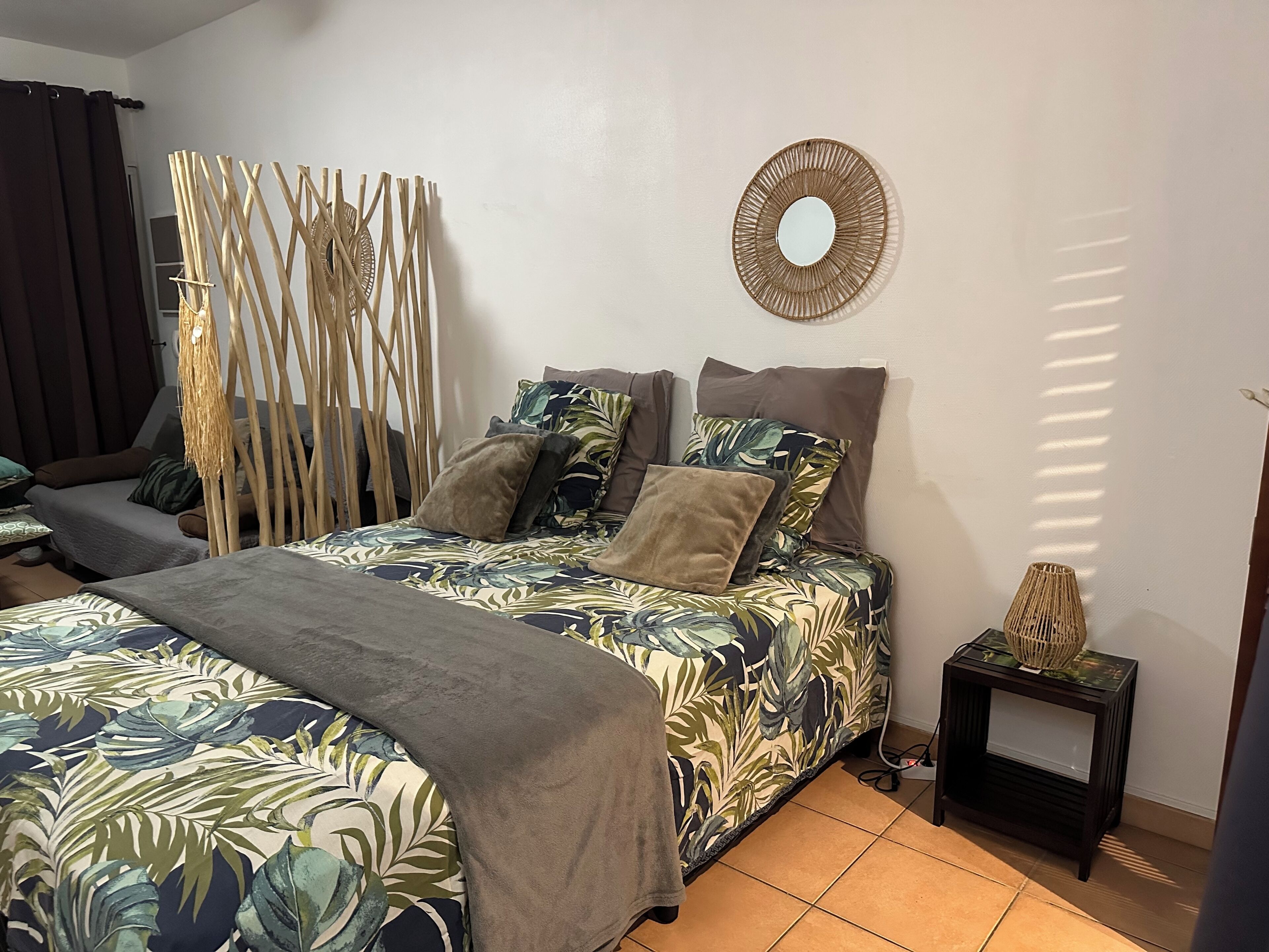 Un dormitorio con cama, mesita de noche, espejo y cortina.
