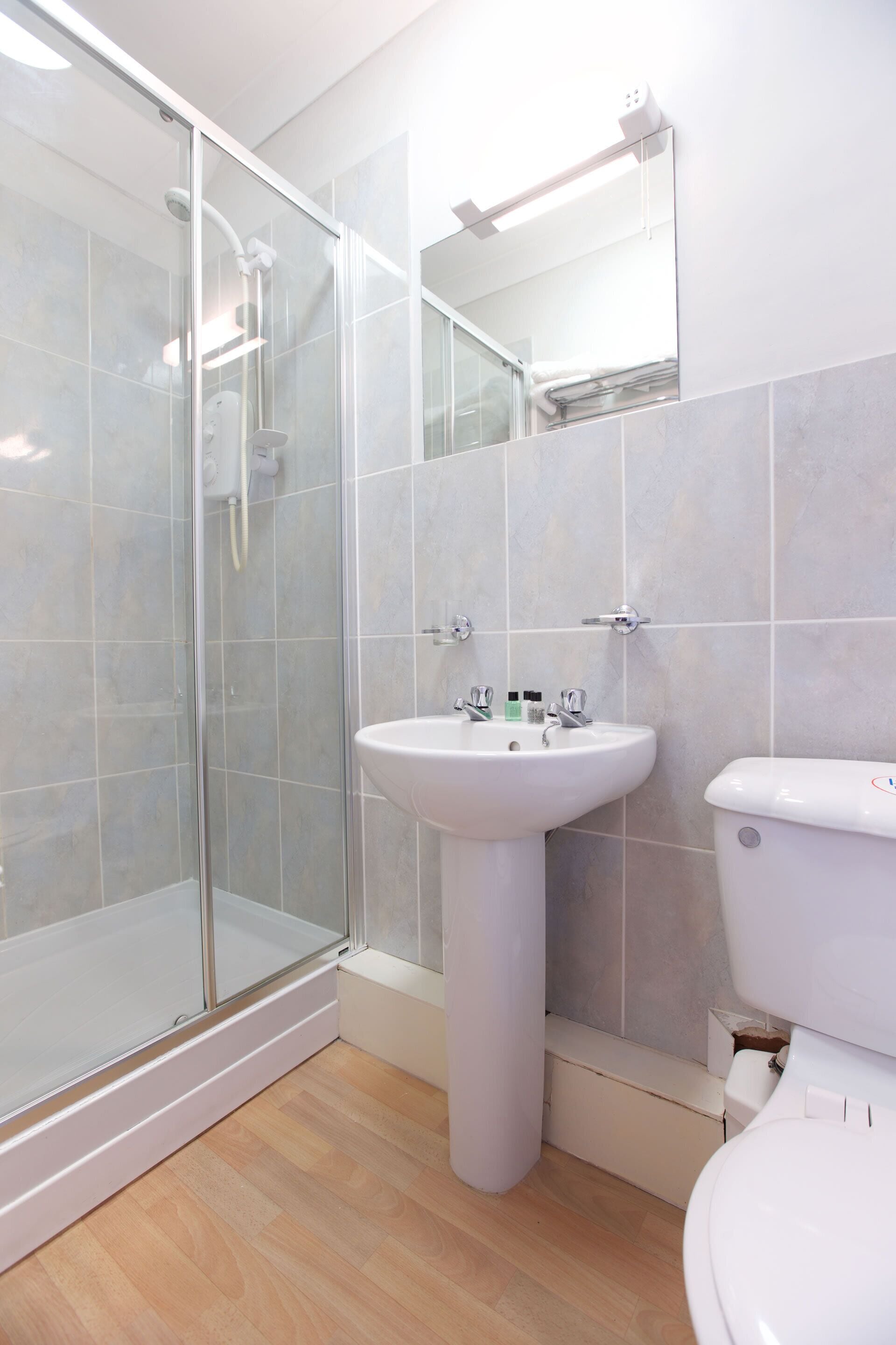 A bathroom with a glass shower enclosure, a pedestal sink, and a toilet.