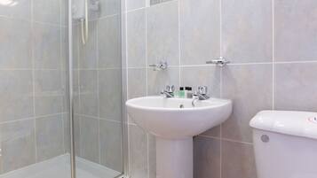 A bathroom with a glass shower enclosure, a pedestal sink, and a toilet.
