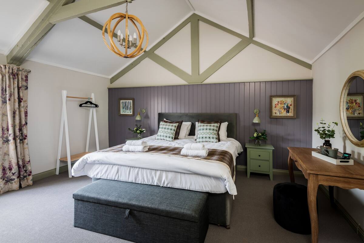 Een slaapkamer met een bed, nachtkastjes, een bureau, een hangstoel en een spiegel.