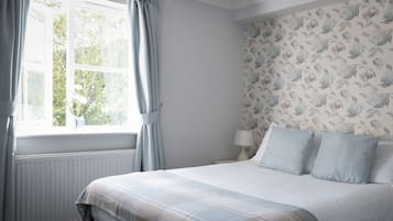 Un dormitorio con cama, ventana con cortinas, radiador y papel tapiz con estampado floral.