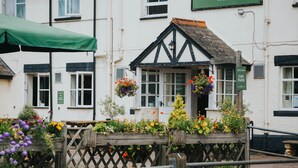 A traditional building with a black timber frame and white walls, featuring a wooden bench with flower baskets and a green awning. - Kings Arms Otterton (Budleigh Salterton)