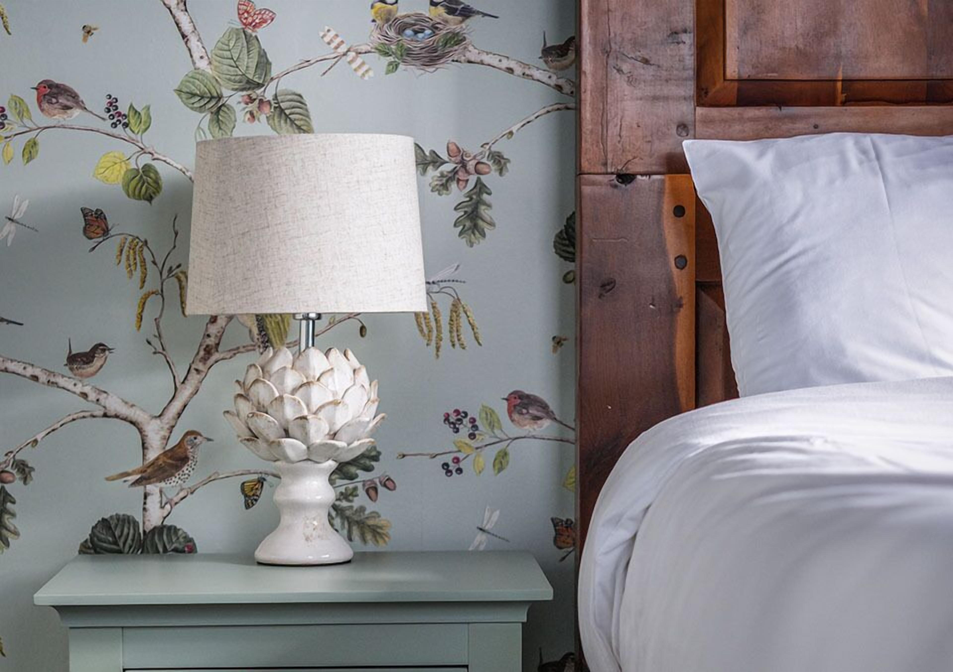 Ein Nachttisch mit Lampe und einer Wand mit Blumenmuster.