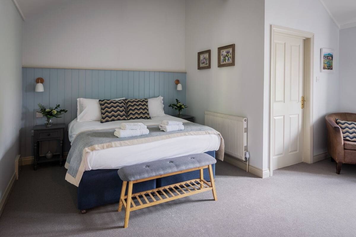 Een slaapkamer met een bed, nachtkastjes, een bankje en een deur.