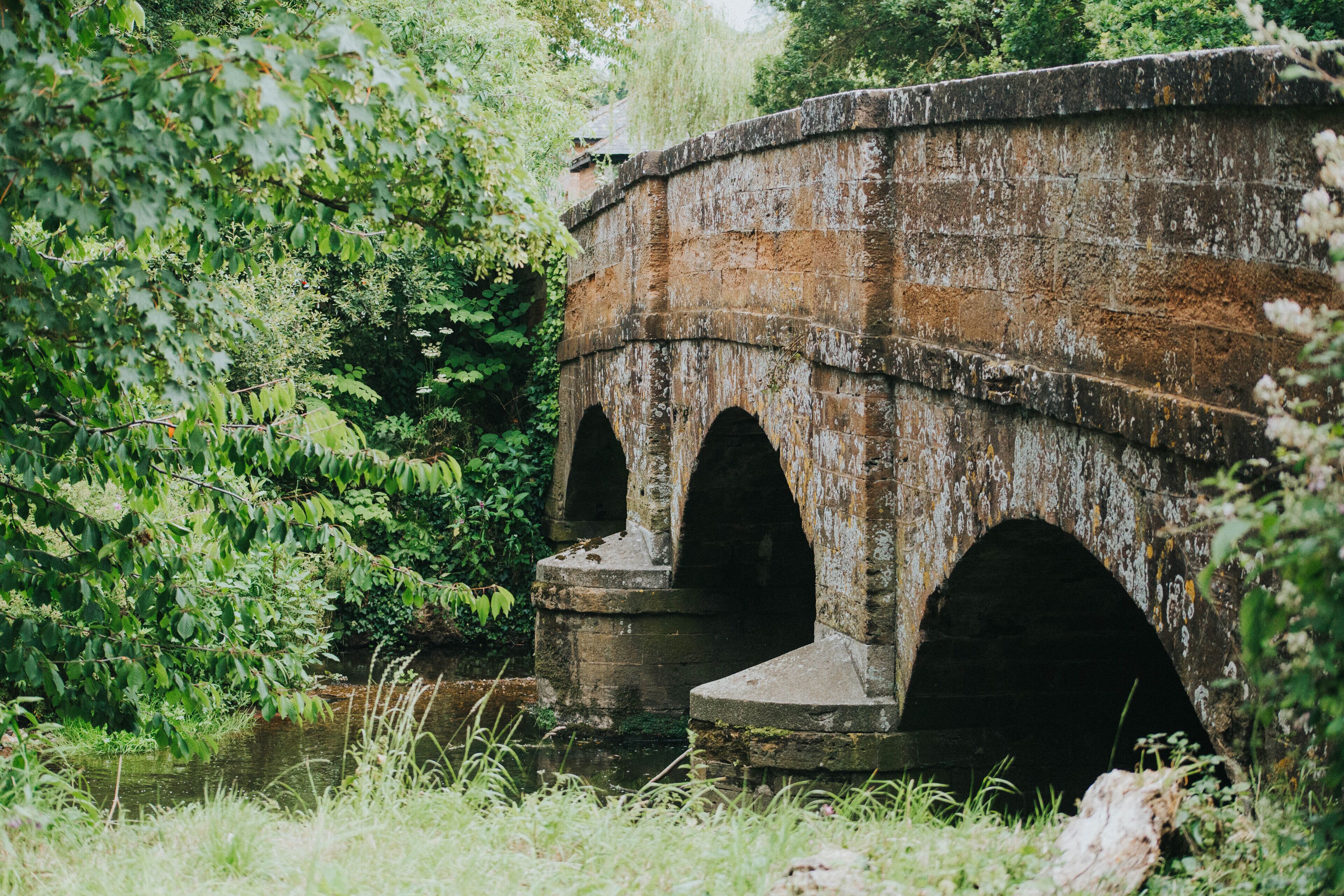 A stone bridge with three arches over a river, surrounded by lush greenery.