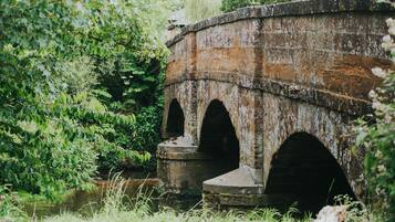 A stone bridge with three arches over a river, surrounded by lush greenery.