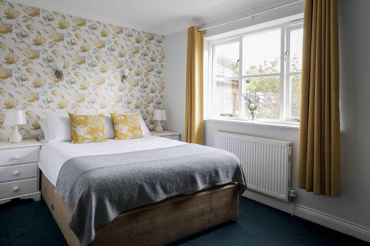 Een slaapkamer met een bed, nachtkastjes, een raam met gordijnen en bloemenbehang.