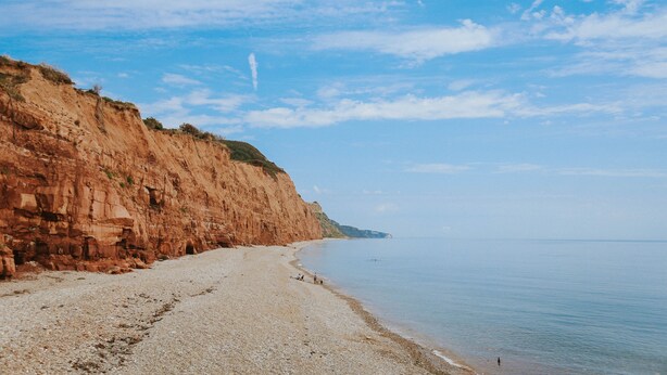 A coastal beach with a rocky cliff and calm sea. - Kings Arms Otterton (Budleigh Salterton)
