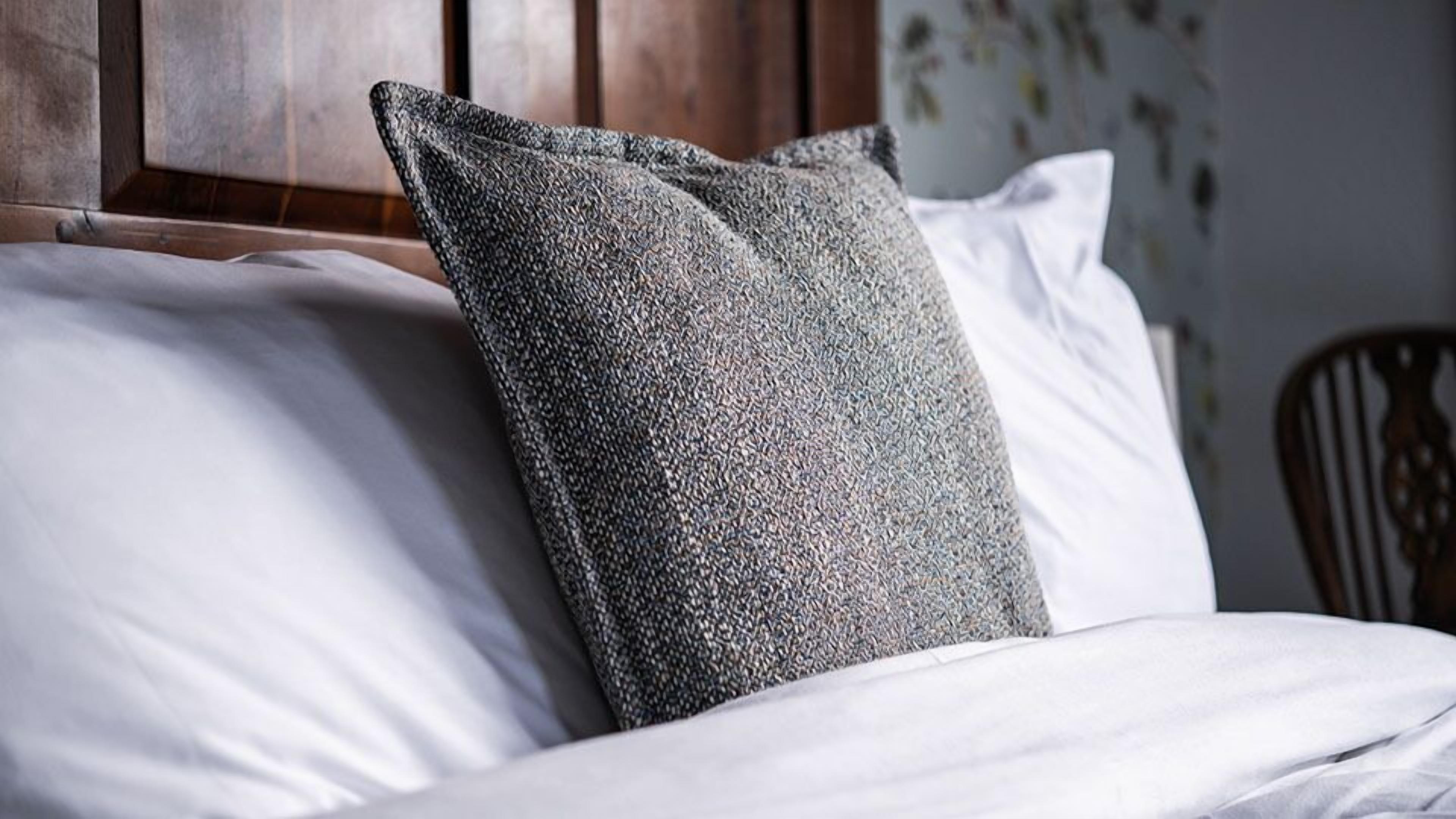 A bed with white bedding and a textured gray pillow.
