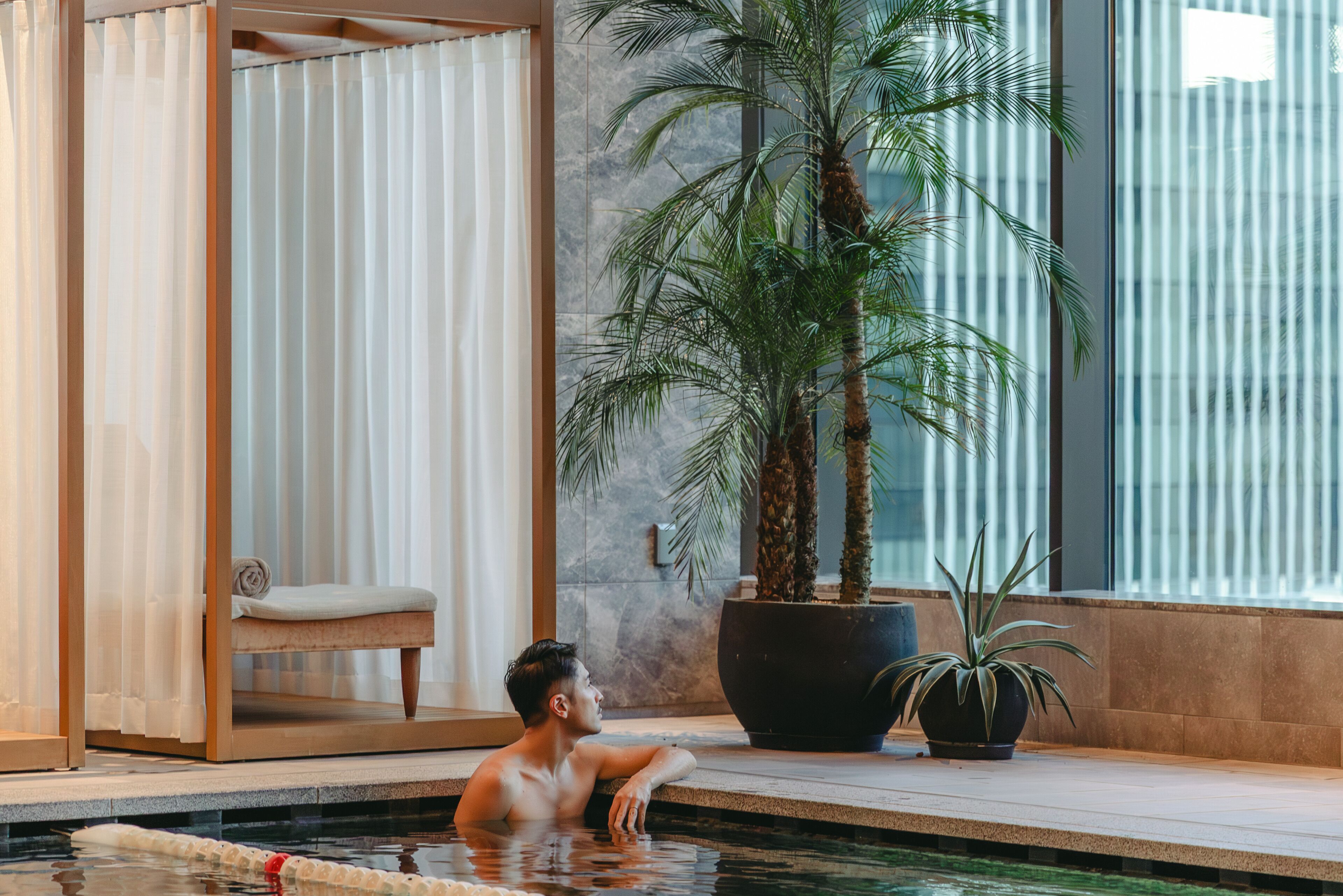 Un hombre en una piscina con una silla y una planta grande en maceta.