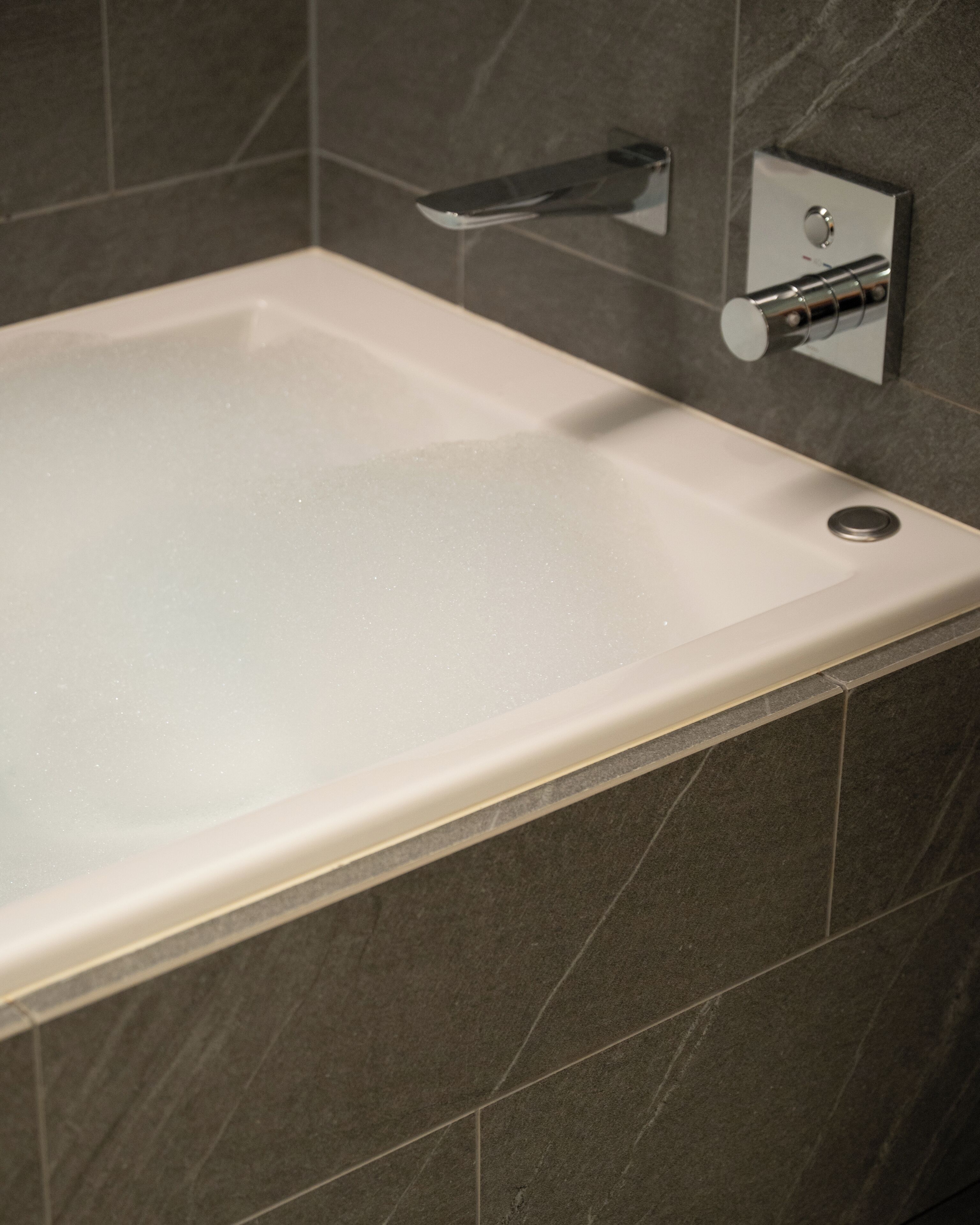 A modern bathroom with a rectangular bathtub, a chrome faucet, and a wall-mounted control panel.