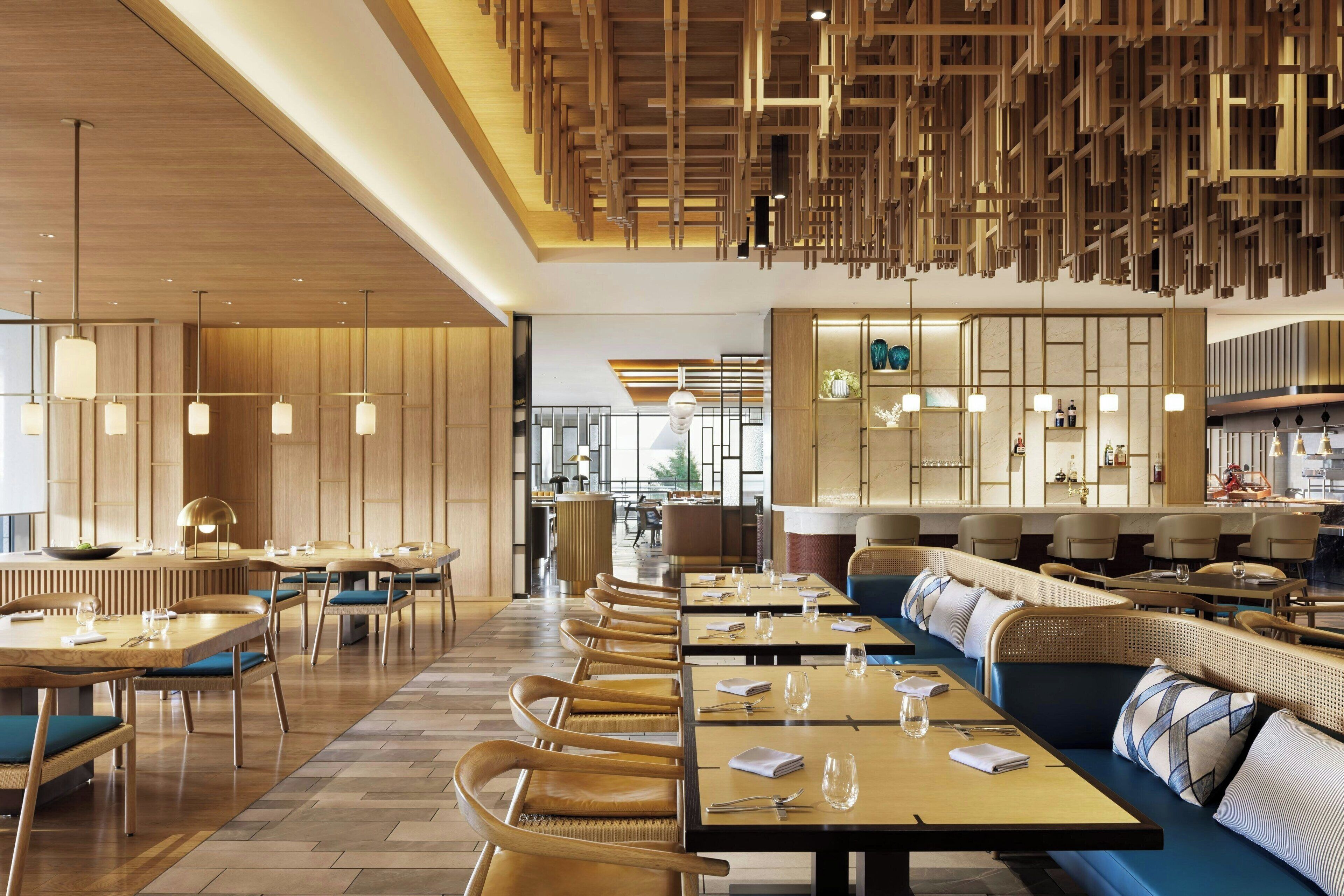Un restaurante moderno con mobiliario de madera, iluminación colgante y una zona de bar central.
