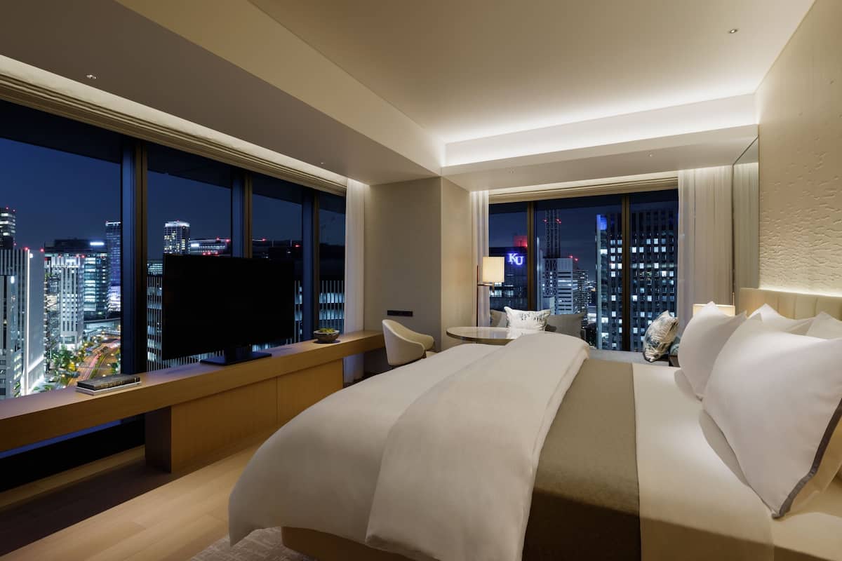 Una habitació d'hotel moderna amb un llit gran, una taula de treball i vista a la ciutat de nit.