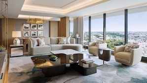 Una sala de estar moderna con un sofá, sillones, una mesa de centro y vistas a la ciudad a través de amplios ventanales.