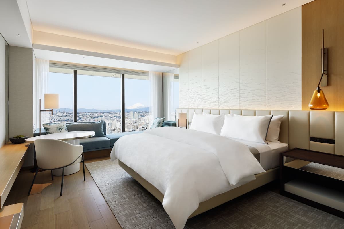 Habitació d'hotel moderna amb un llit gran, una taula de treball i vista a un paisatge urbà.