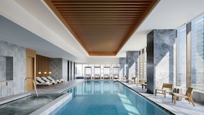 Una piscina interior moderna con sillones de descanso y techo de madera.