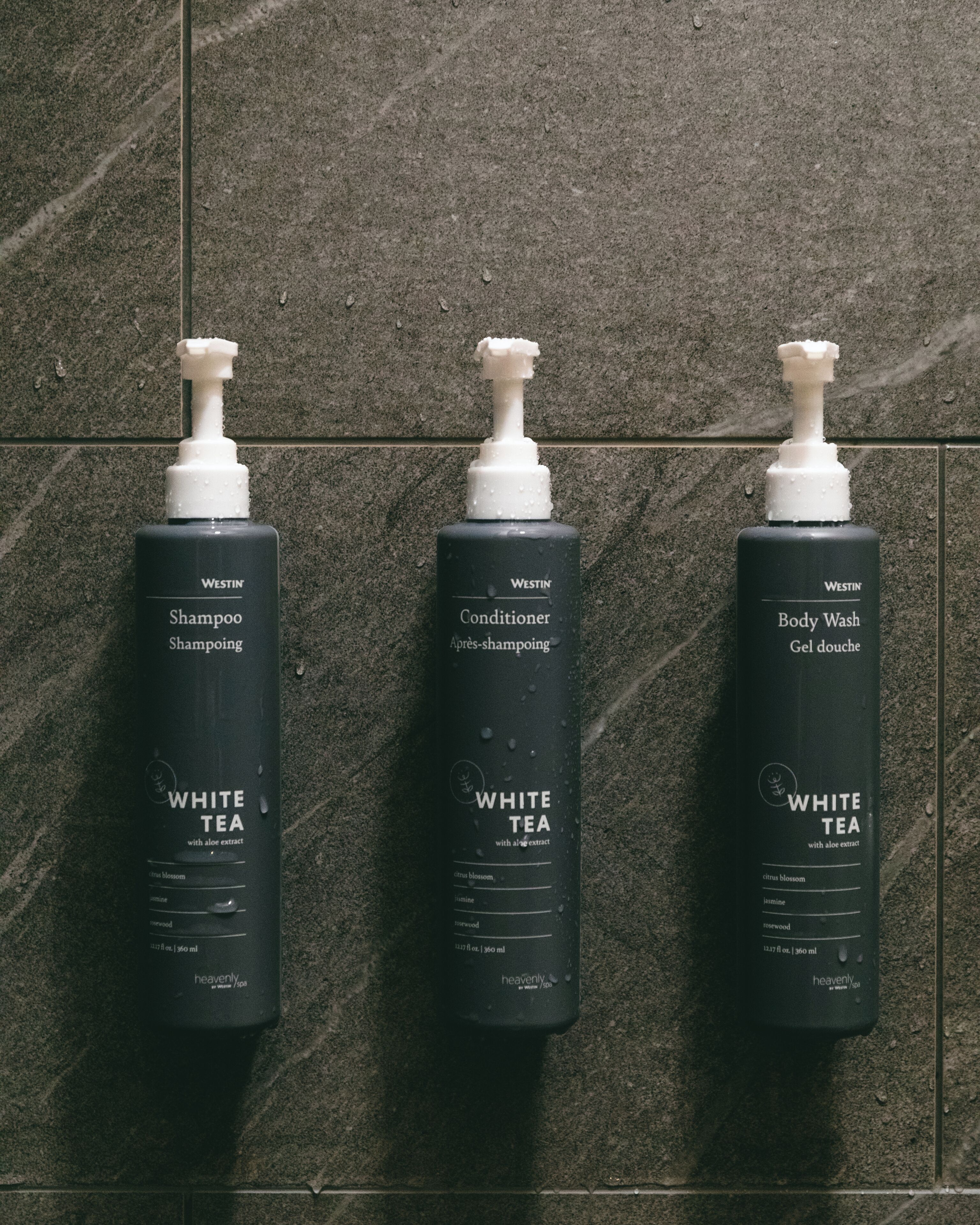 Three bottles of Westin White Tea shampoo, conditioner, and body wash arranged against a tiled wall.