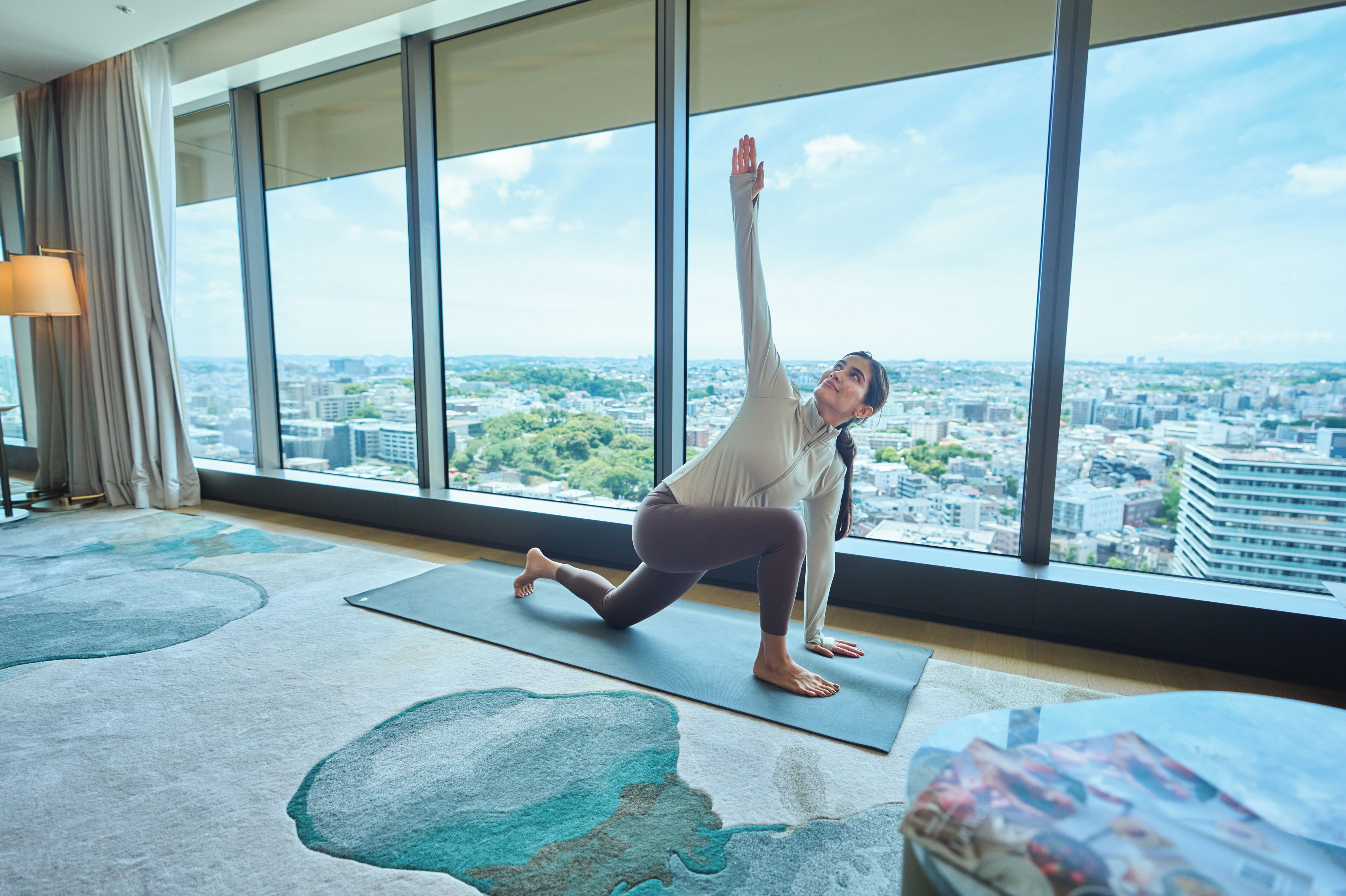 A person performing a yoga pose on a mat in a room with large windows overlooking a cityscape.