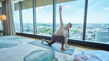 A person performing a yoga pose on a mat in a room with large windows overlooking a cityscape.