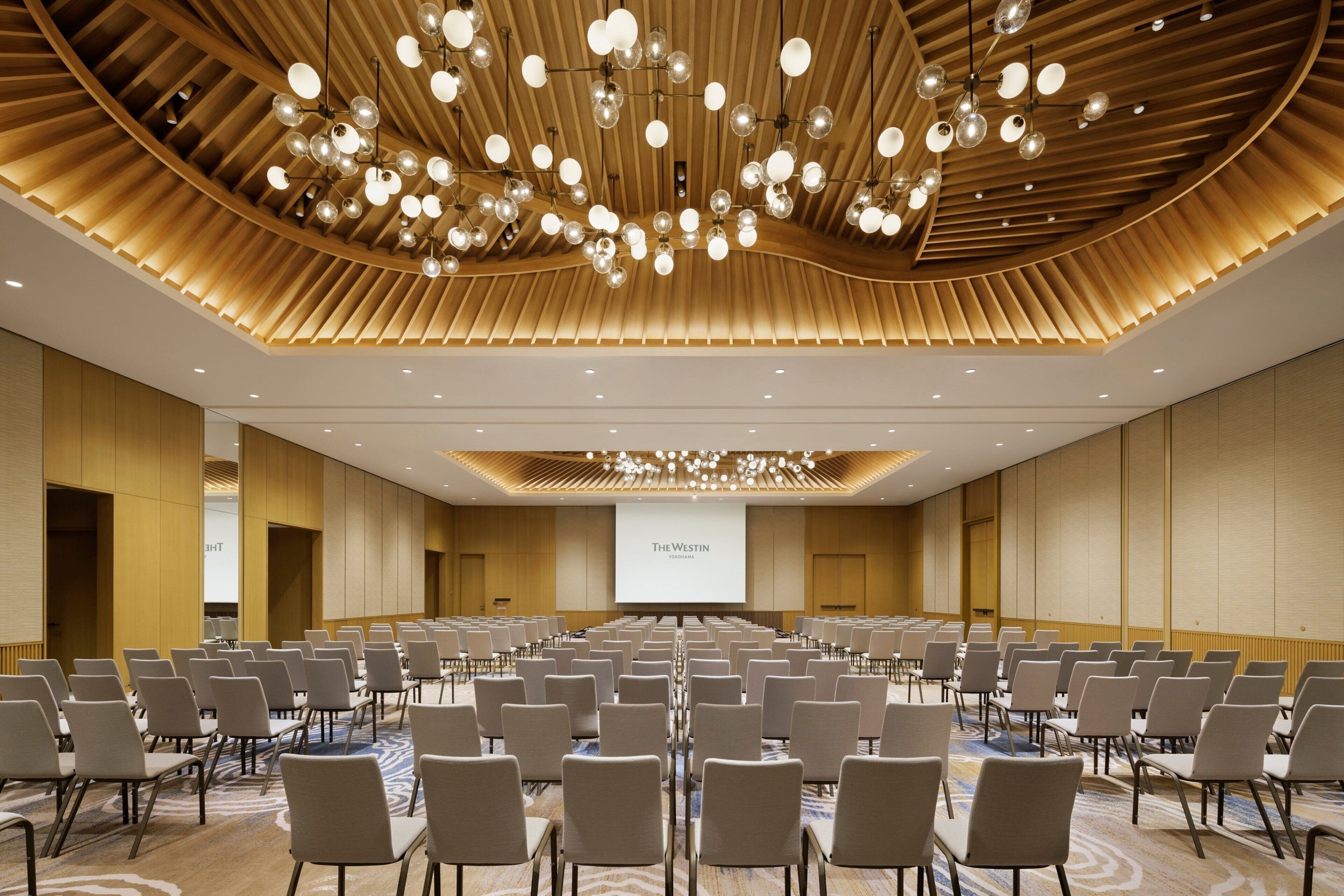 A conference room with rows of chairs, a large screen, and a modern ceiling design.
