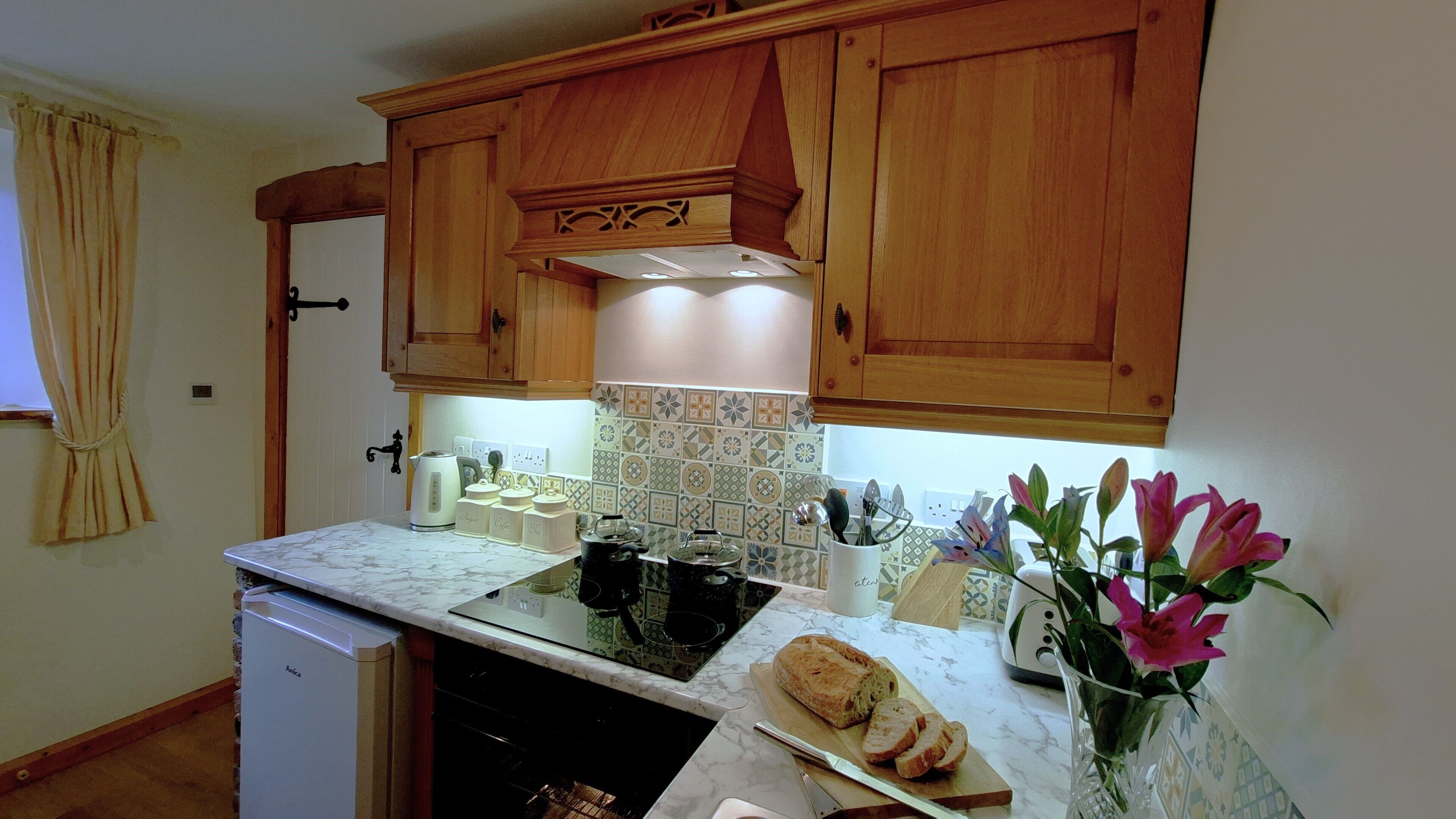 A kitchen with wooden cabinets, a built-in stove, a white refrigerator, and a countertop with a bread loaf and a vase of flowers.