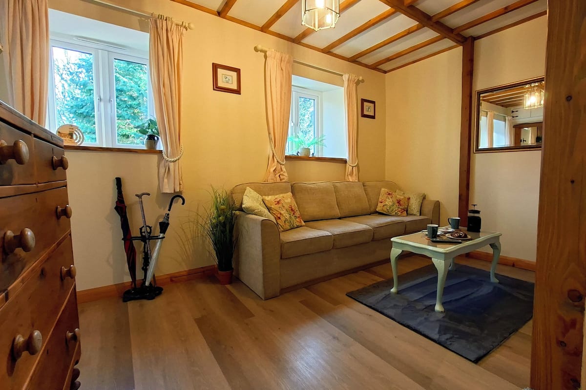 A cozy room with a wooden floor, a sofa, a small table, and a window with curtains.