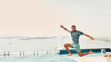 Un homme saute dans une piscine, avec une vue sur la ville en arrière-plan.