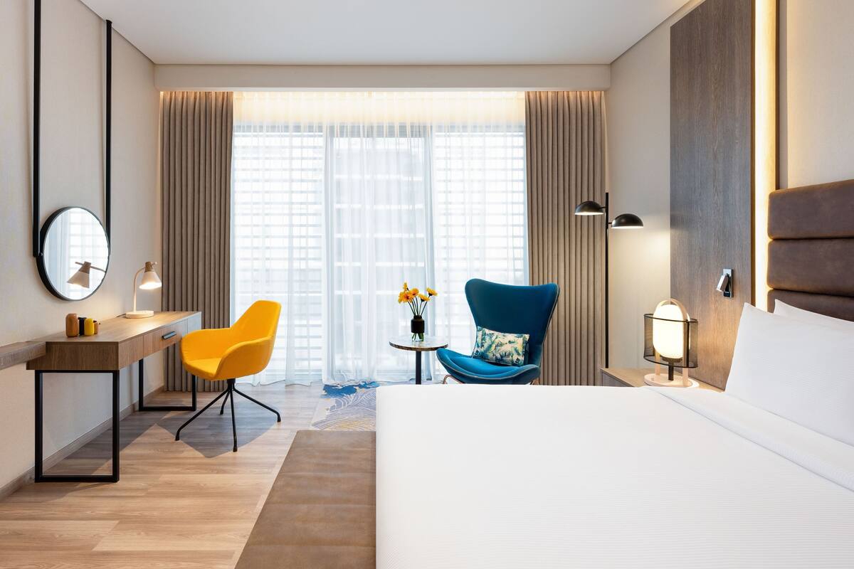 Une chambre d’hôtel équipée d’un lit, d’un bureau, d’une chaise, d’une télévision, d’une lampe et d’une fenêtre avec des rideaux.