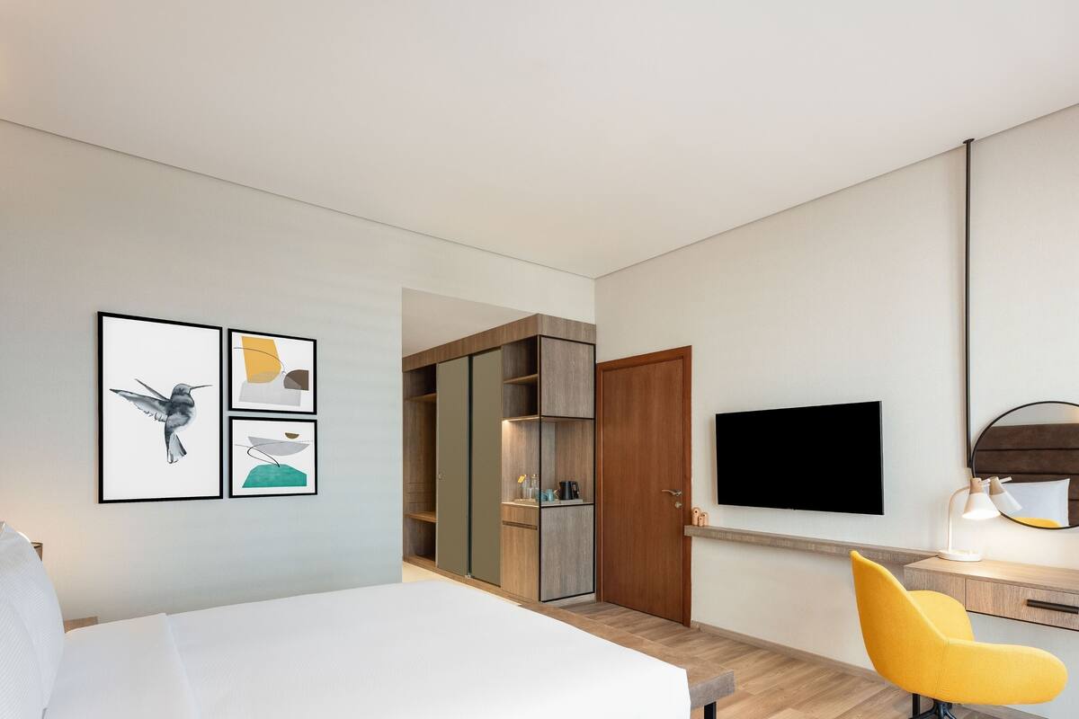 Une chambre d’hôtel moderne équipée d’un lit, d’un bureau avec une chaise, d’une télévision et d’une armoire.