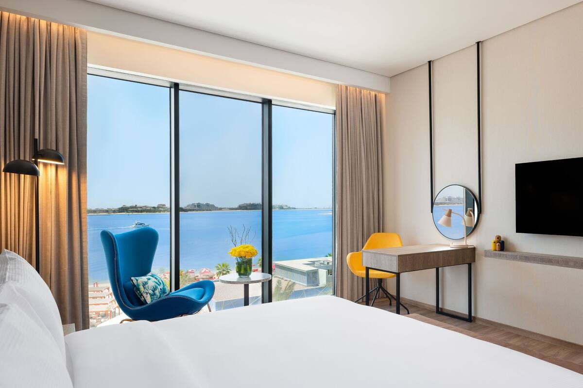 Une chambre d’hôtel avec un grand lit, un bureau, une chaise, une télévision et une vue sur la mer.