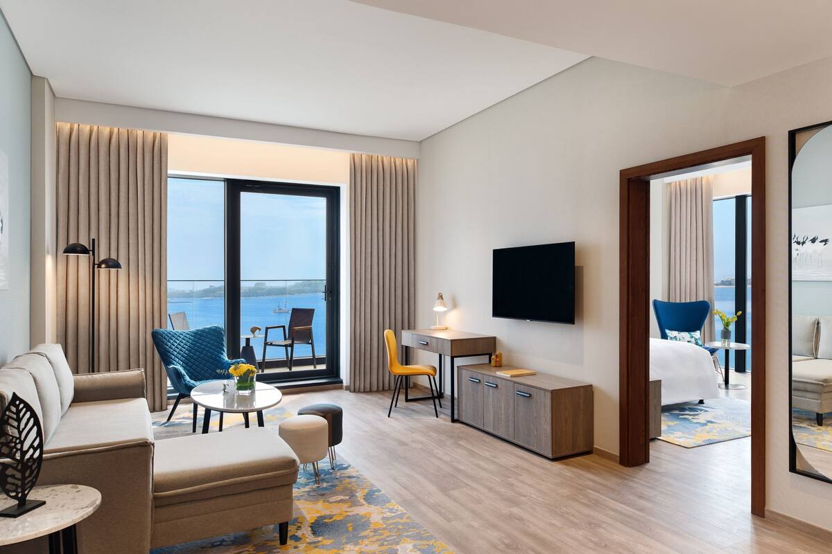 Une chambre d’hôtel moderne dotée d’un balcon, d’une télévision à écran plat, d’un bureau avec une lampe et d’un canapé.