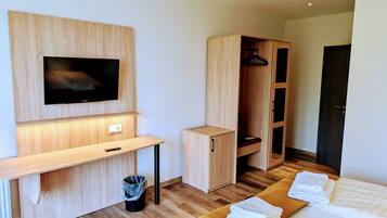 Una habitación de hotel moderna con un escritorio de madera, un televisor montado en la pared, un armario y una cama con toallas ordenadas.