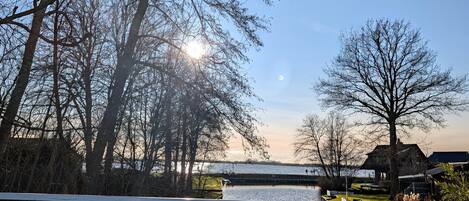 A riverside view with a wooden bridge, bare trees, and a distant building.