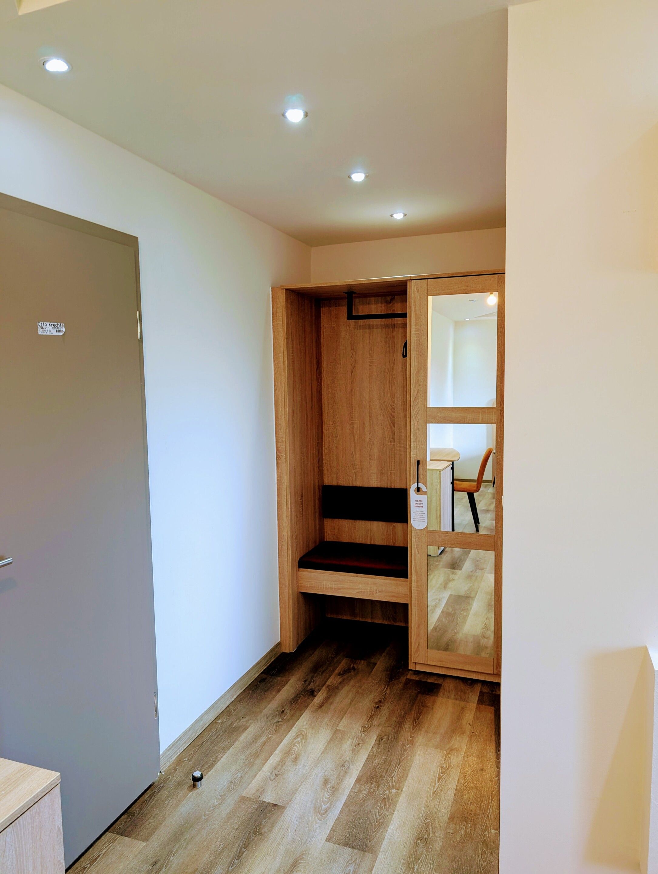 A room with a wooden wardrobe, a grey door, and a wooden floor.
