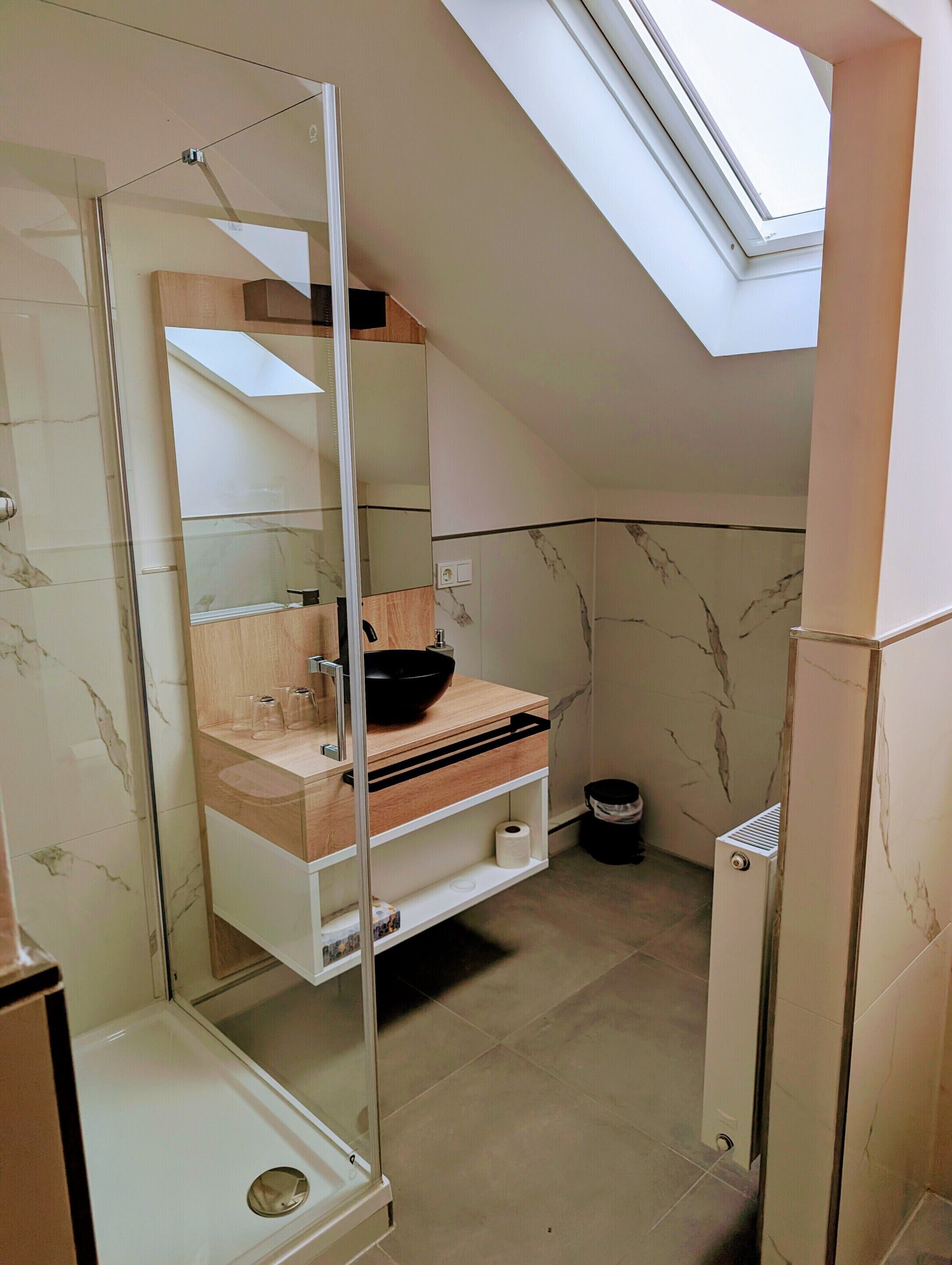 Un baño moderno con cabina de ducha de vidrio, tocador de madera y salpicadero de mármol.