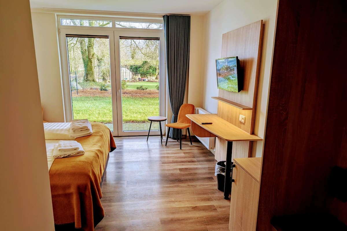 A hotel room with two beds, a desk, a chair, a TV, and a view of the outdoors.