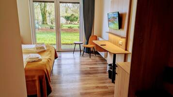 A hotel room with two beds, a desk, a chair, a TV, and a view of the outdoors.
