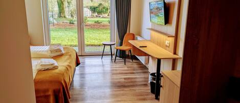 Een hotelkamer met twee bedden, een bureau, een stoel, een televisie en uitzicht op de omgeving.