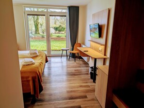A hotel room with two beds, a desk, a chair, a TV, and a view of the outdoors. - Hotel Tausendschön (Sudbrookmerland)