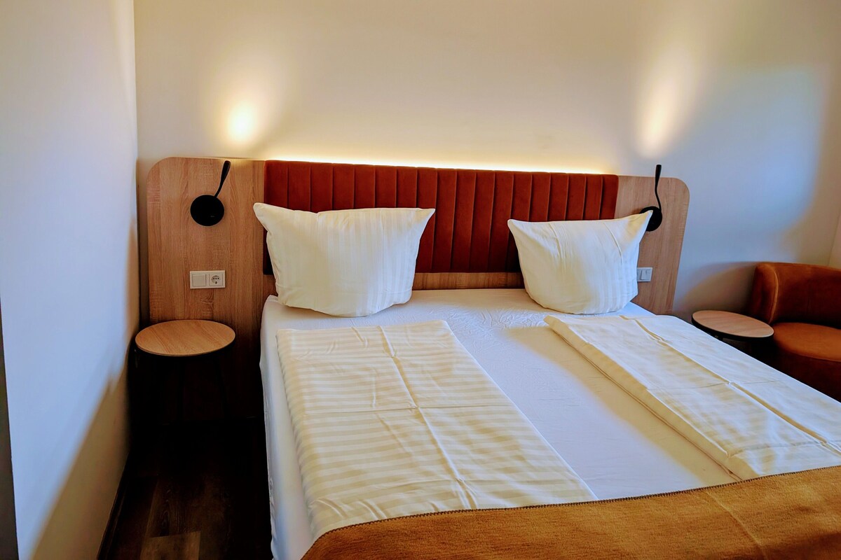 A hotel room with a large bed, two bedside tables, a wooden headboard, and a small seating area.