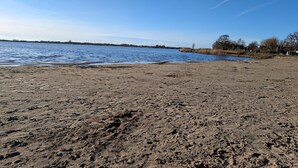 A sandy beach with a calm body of water, a clear sky, and distant wind turbines. - Hotel Tausendschön (Sudbrookmerland)