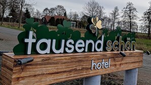 A wooden sign with the words "tausend schon hotel" and clover decorations. - Hotel Tausendschön (Sudbrookmerland)